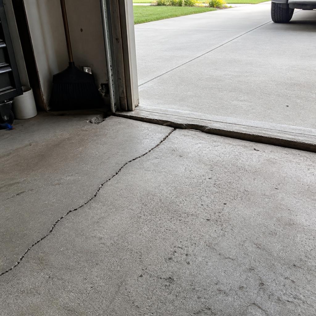Settled residential garage floor in Albuquerque, NM with a visible crack and dropped slab section near the overhead door